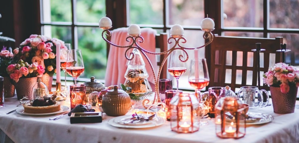 A dining table set up with a pink table cloth, plates, and pink accent flowers, and other decorations