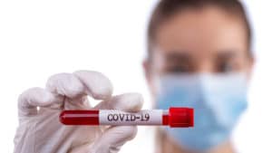 blurred photo of a women with it focus on a vile that says COVID-19